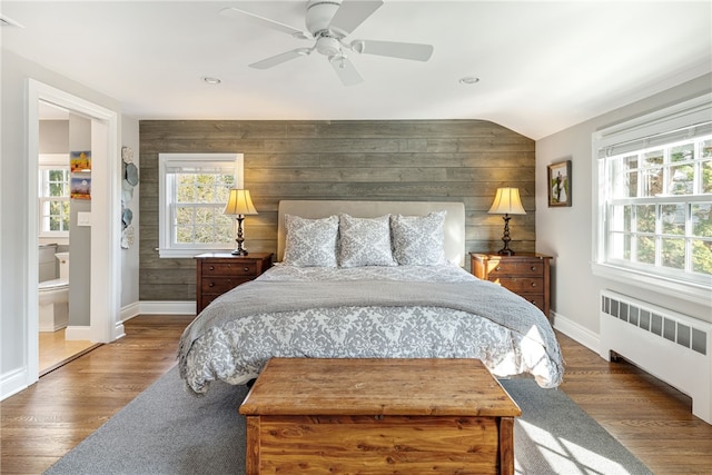 bedroom with wooden walls, radiator, wood finished floors, lofted ceiling, and ceiling fan