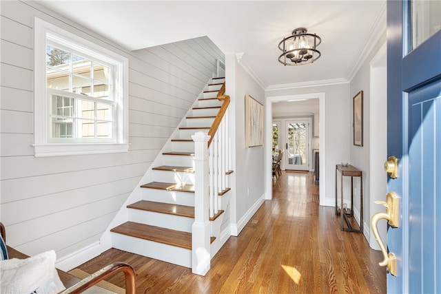 entryway with ornamental molding, wood finished floors, baseboards, a chandelier, and stairs