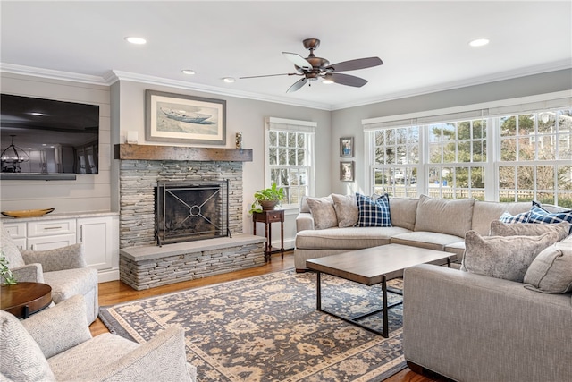 living area featuring ornamental molding, wood finished floors, recessed lighting, a stone fireplace, and ceiling fan