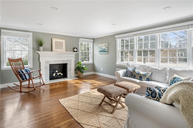 living area with a fireplace with flush hearth, crown molding, baseboards, and wood finished floors