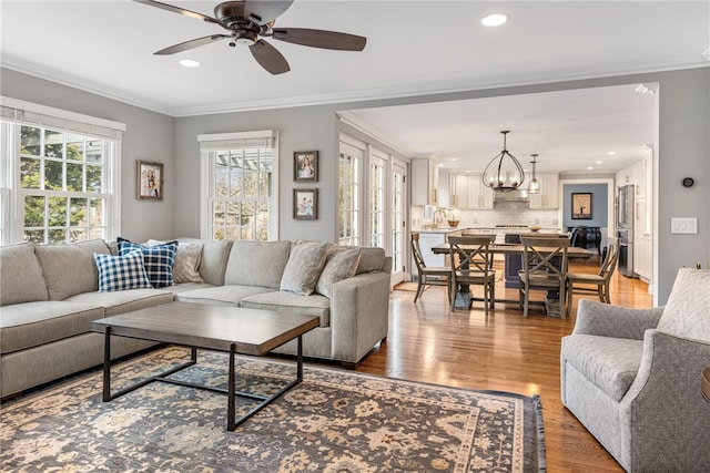 living room featuring recessed lighting, ceiling fan with notable chandelier, light wood-style floors, and ornamental molding