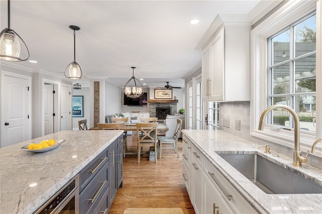 kitchen with ornamental molding, light stone counters, light wood-style flooring, white cabinets, and a sink