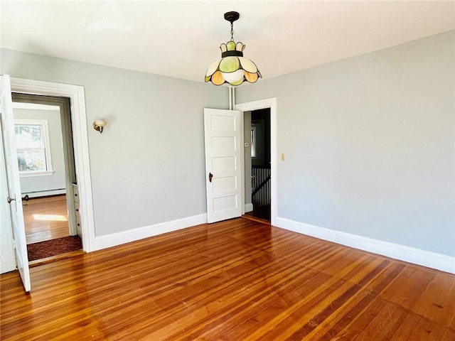 spare room with a baseboard radiator, baseboards, and wood finished floors