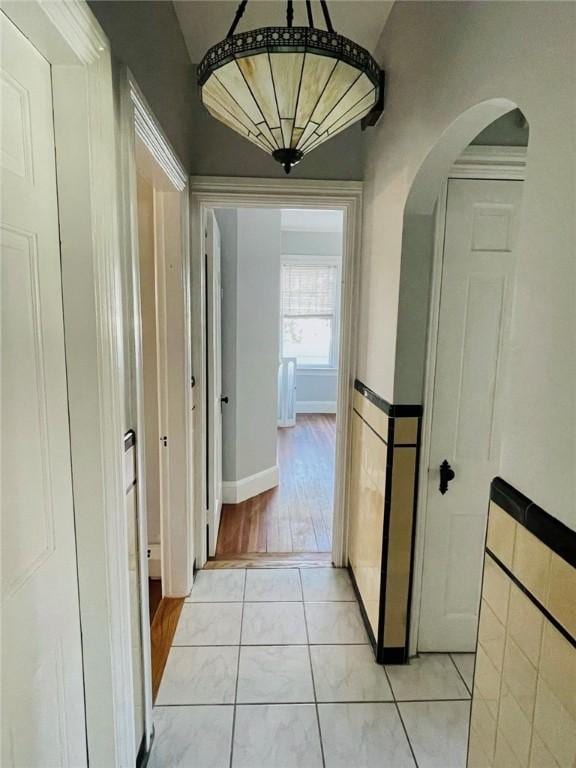 hallway with arched walkways, wainscoting, tile walls, and light tile patterned floors