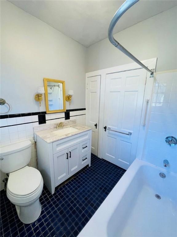 bathroom with wainscoting, toilet, bathtub / shower combination, vanity, and tile walls