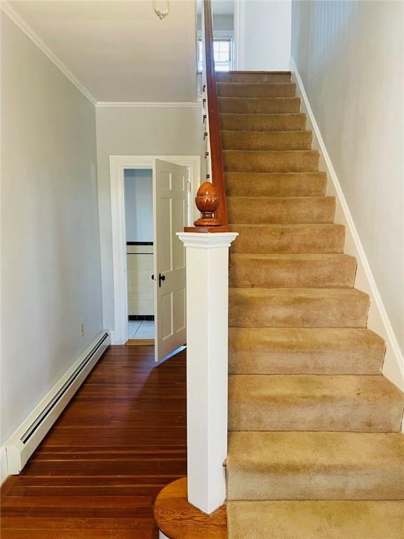 staircase with crown molding, baseboard heating, and wood finished floors