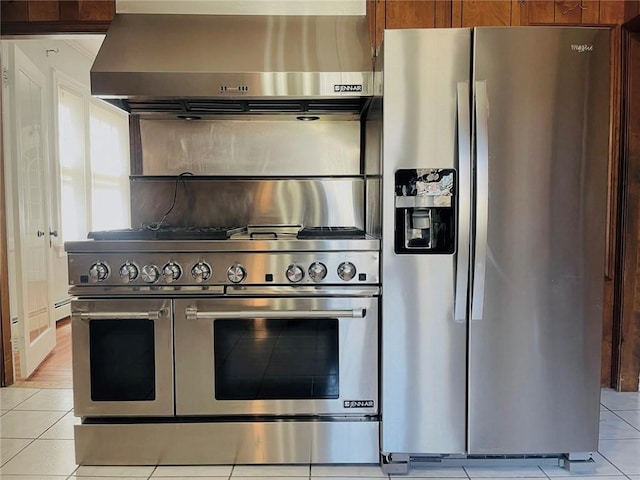 kitchen featuring light tile patterned floors, stainless steel appliances, wall chimney range hood, and brown cabinetry