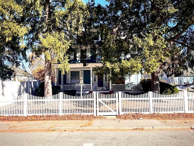 view of property hidden behind natural elements featuring a fenced front yard and a porch