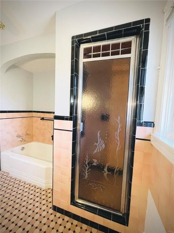 bathroom with a stall shower, tile patterned floors, tile walls, and a bath