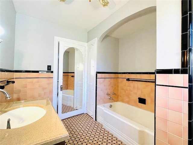 full bath with wainscoting, tile walls, vanity, and a bath