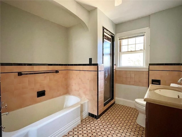 bathroom featuring toilet, a wainscoted wall, vanity, tile walls, and a bath