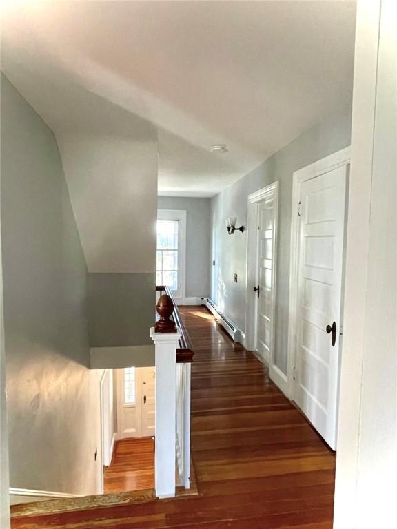 corridor featuring a baseboard heating unit, wood finished floors, and an upstairs landing