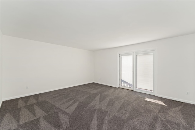 empty room featuring visible vents, dark carpet, and baseboards