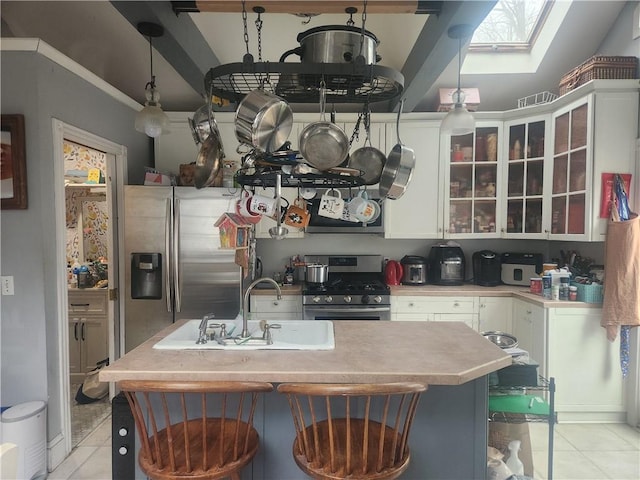 kitchen featuring a skylight, white cabinets, appliances with stainless steel finishes, light countertops, and a sink