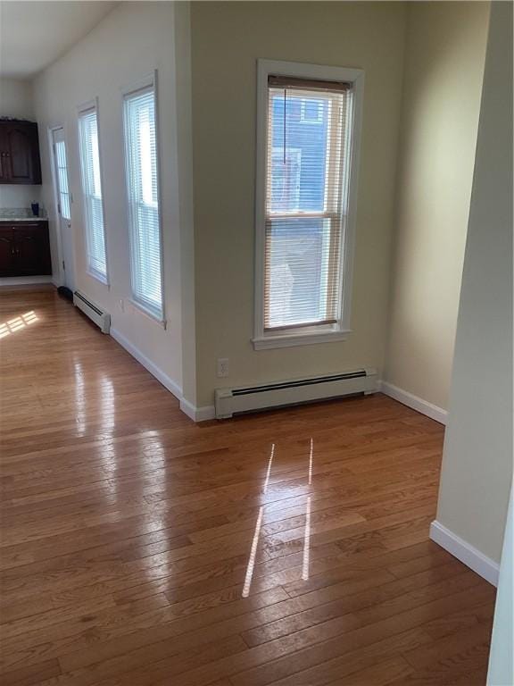 interior space with a baseboard heating unit, baseboards, and light wood finished floors