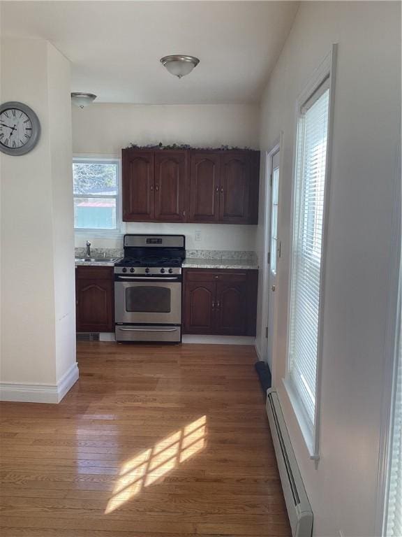 kitchen with stainless steel range with gas stovetop, baseboard heating, light countertops, light wood-style floors, and a sink