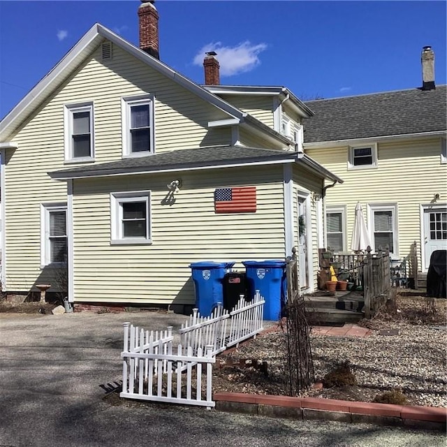 back of property with a chimney and roof with shingles