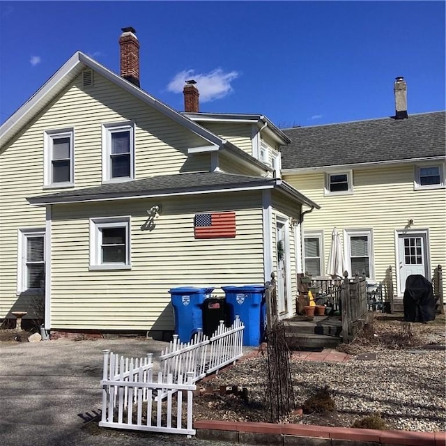 rear view of property featuring a shingled roof and a chimney