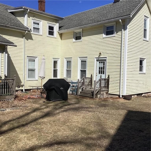 back of house with a chimney and roof with shingles