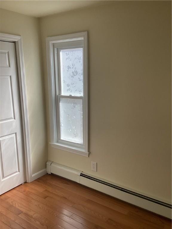 spare room featuring baseboard heating, light wood-type flooring, and baseboards