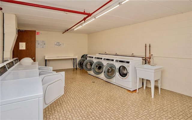 community laundry room featuring concrete block wall, light floors, washer and clothes dryer, and stacked washer / drying machine