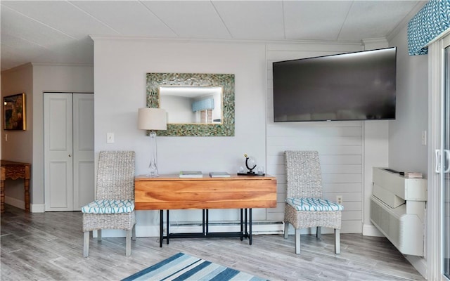 living area featuring baseboards, a baseboard heating unit, wood finished floors, and crown molding