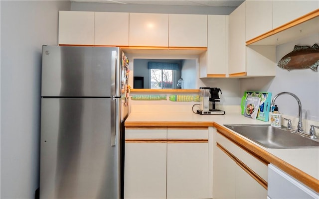 kitchen with dishwasher, light countertops, a sink, and freestanding refrigerator