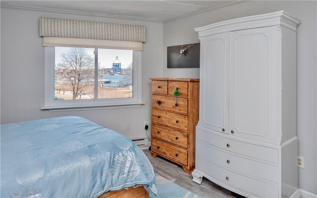 bedroom with light wood-type flooring, a baseboard radiator, and ornamental molding