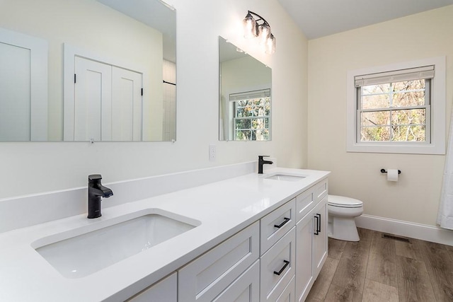 bathroom featuring double vanity, a sink, toilet, and wood finished floors