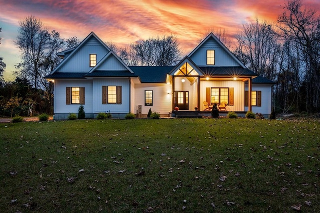 back of property at dusk featuring a porch, a lawn, and a shingled roof