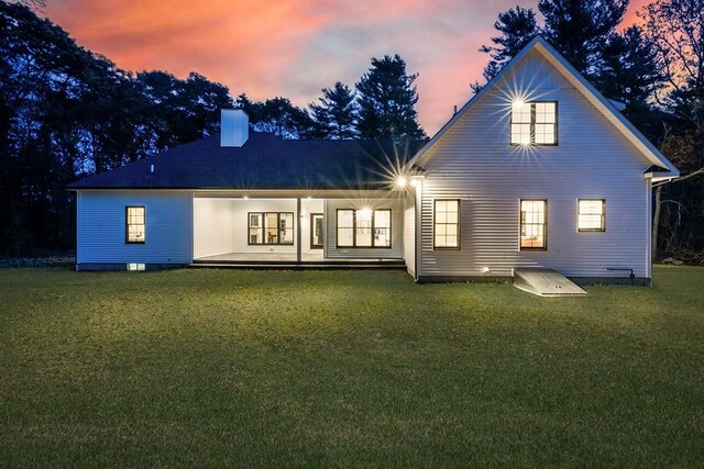 back of property at dusk with a lawn and a chimney