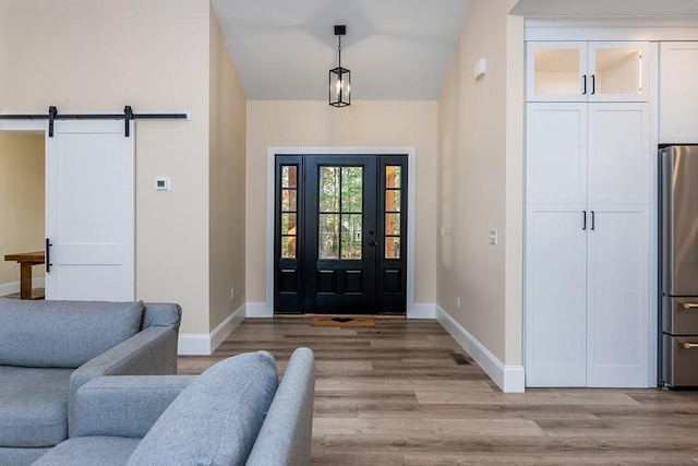 entrance foyer featuring lofted ceiling, a barn door, baseboards, and light wood-style flooring