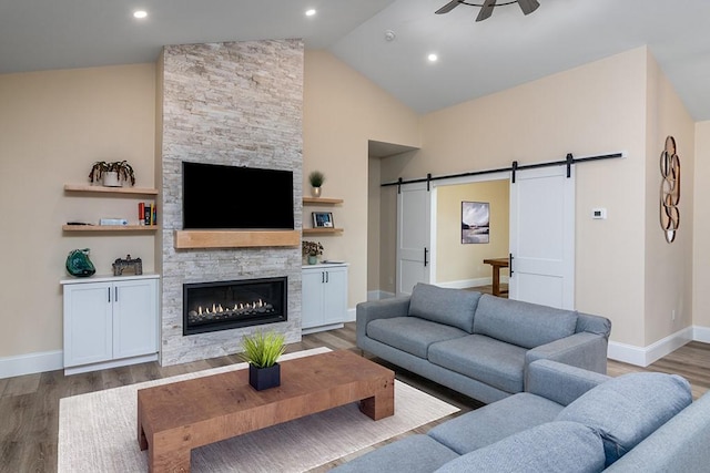 living area featuring a fireplace, a barn door, vaulted ceiling, ceiling fan, and wood finished floors