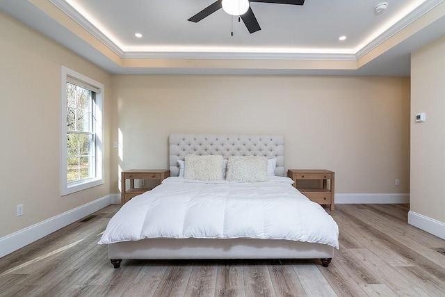 bedroom featuring ornamental molding, a raised ceiling, baseboards, and wood finished floors