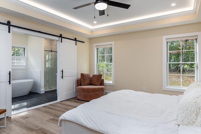 bedroom featuring a barn door, multiple windows, a raised ceiling, and wood finished floors