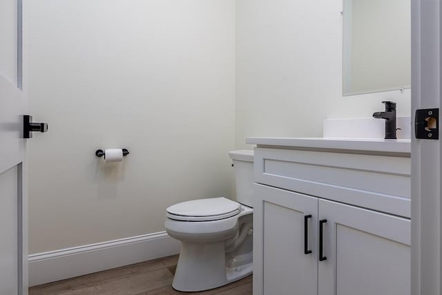 half bath featuring vanity, toilet, and wood finished floors