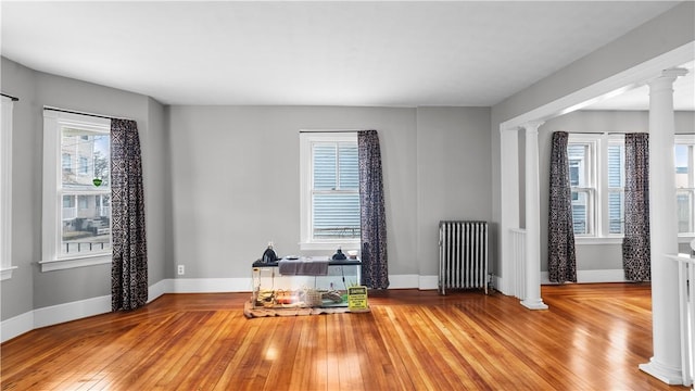 unfurnished room featuring radiator, decorative columns, baseboards, and hardwood / wood-style floors