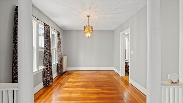 empty room with radiator heating unit, baseboards, a notable chandelier, and light wood finished floors