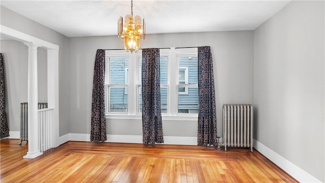 unfurnished room featuring baseboards, radiator heating unit, light wood-type flooring, and ornate columns