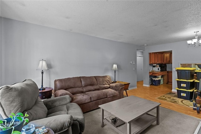 living room featuring baseboards, a textured ceiling, an inviting chandelier, and light wood finished floors