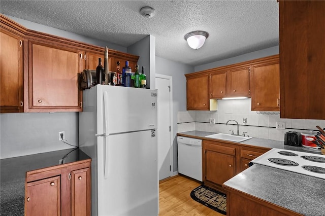 kitchen with tasteful backsplash, light wood-style floors, brown cabinetry, white appliances, and a sink