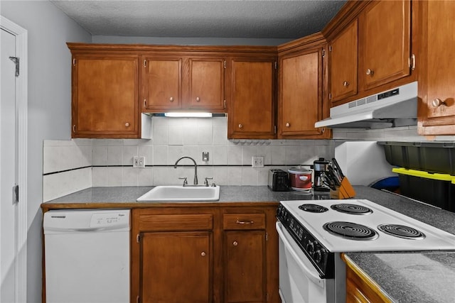 kitchen with backsplash, under cabinet range hood, brown cabinetry, white appliances, and a sink