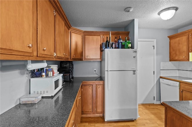 kitchen with white appliances, dark countertops, light wood-style flooring, and brown cabinetry