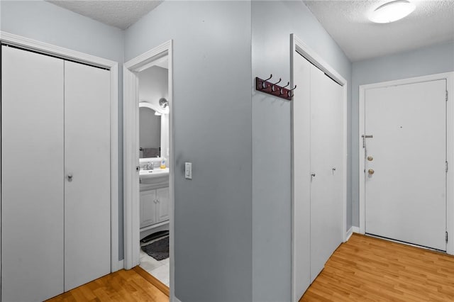 hall featuring a sink, light wood-type flooring, and a textured ceiling