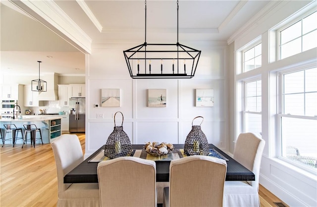 dining room featuring light wood finished floors, a decorative wall, and crown molding