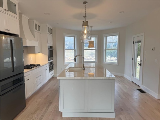 kitchen with custom exhaust hood, visible vents, stainless steel gas stovetop, freestanding refrigerator, and light wood-type flooring