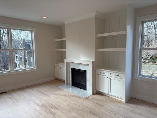 unfurnished living room with built in features, a high end fireplace, light wood-type flooring, and baseboards