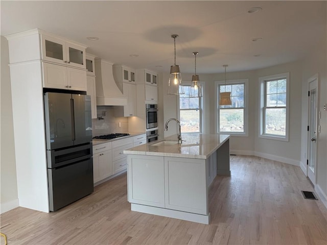 kitchen with light wood-style flooring, premium range hood, a sink, white cabinetry, and appliances with stainless steel finishes