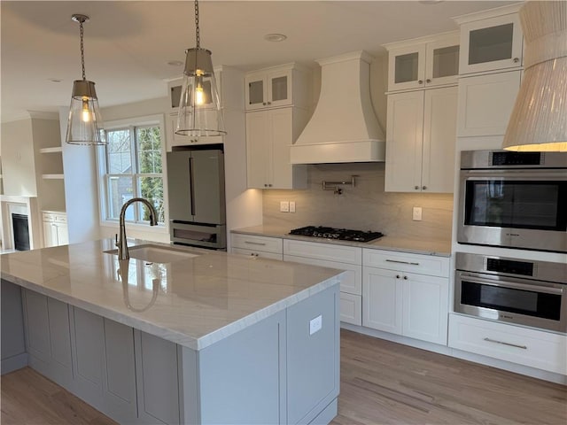 kitchen featuring black gas stovetop, a sink, freestanding refrigerator, an island with sink, and custom range hood