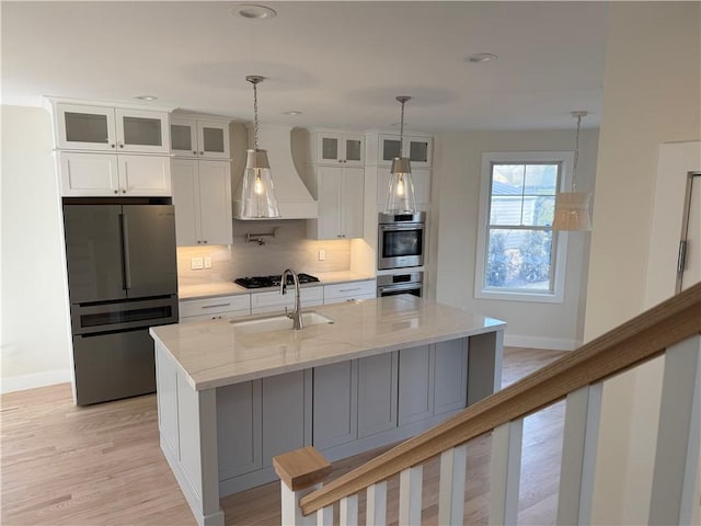 kitchen with custom range hood, decorative backsplash, appliances with stainless steel finishes, white cabinets, and a sink